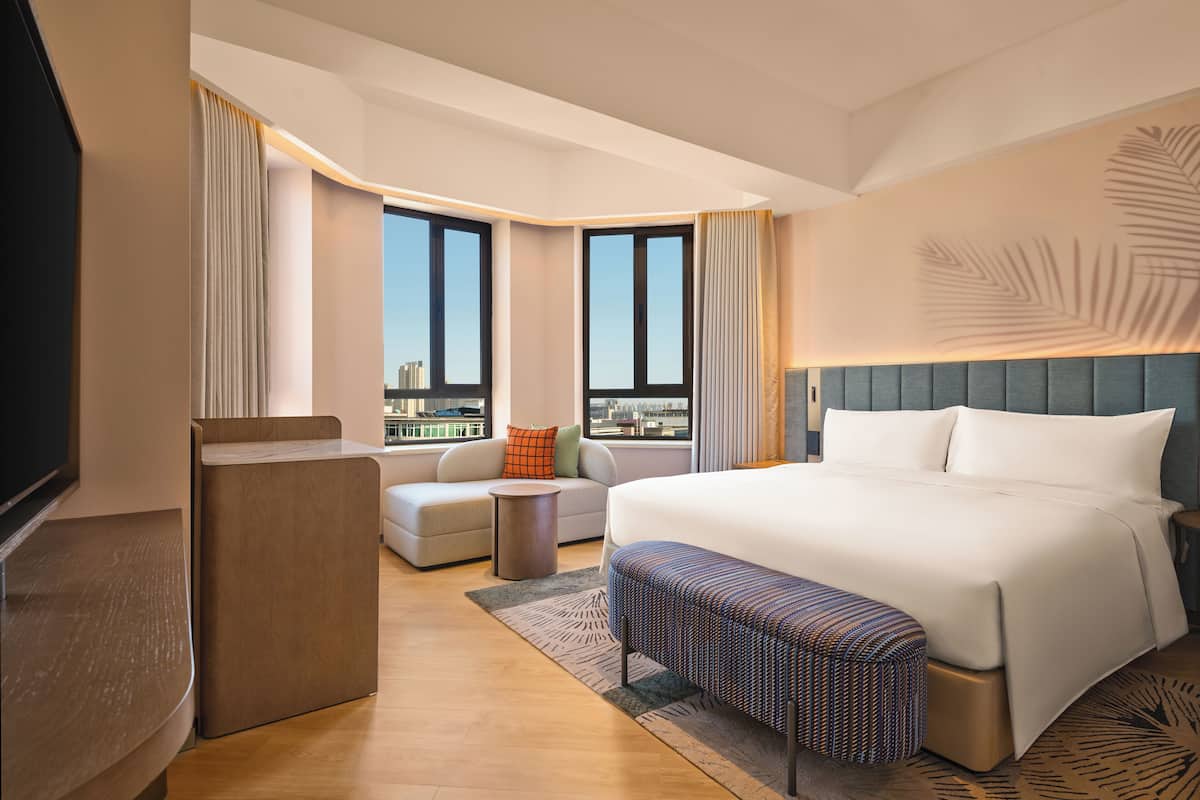 Una habitación de hotel moderna con una cama grande, un sofá, una mesita y un televisor.