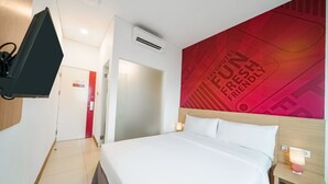 A hotel room with a bed, a TV mounted on the wall, a red wall with text, and a door leading to another room.