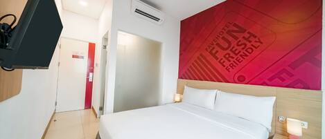 A hotel room with a bed, a TV mounted on the wall, a red wall with text, and a door leading to another room.