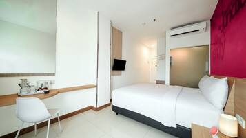 A hotel room with a bed, a desk, a chair, a TV, and an air conditioning unit.