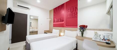 A hotel room with two beds, a desk with a chair, a TV mounted on the wall, and a red wall with the text 'FAVEHOTEL FUN FRESH FRIENDLY'.