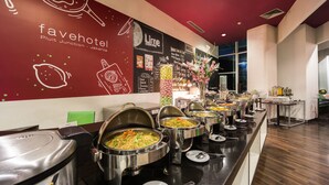 A buffet setup with various food items in large pots, a wall with the hotel's name and location, and a window providing natural light.