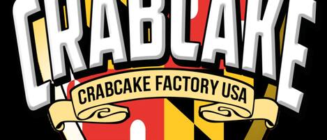 A logo with the text "CRABCAKE" and "CRABCAKE FACTORY USA" on a shield-shaped background with a red cross and stripes.