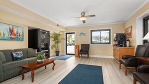 Ein Wohnzimmer mit einer Couch, Couchtisch und Sesseln, einem Deckenventilator und Blick durch eine Tür.