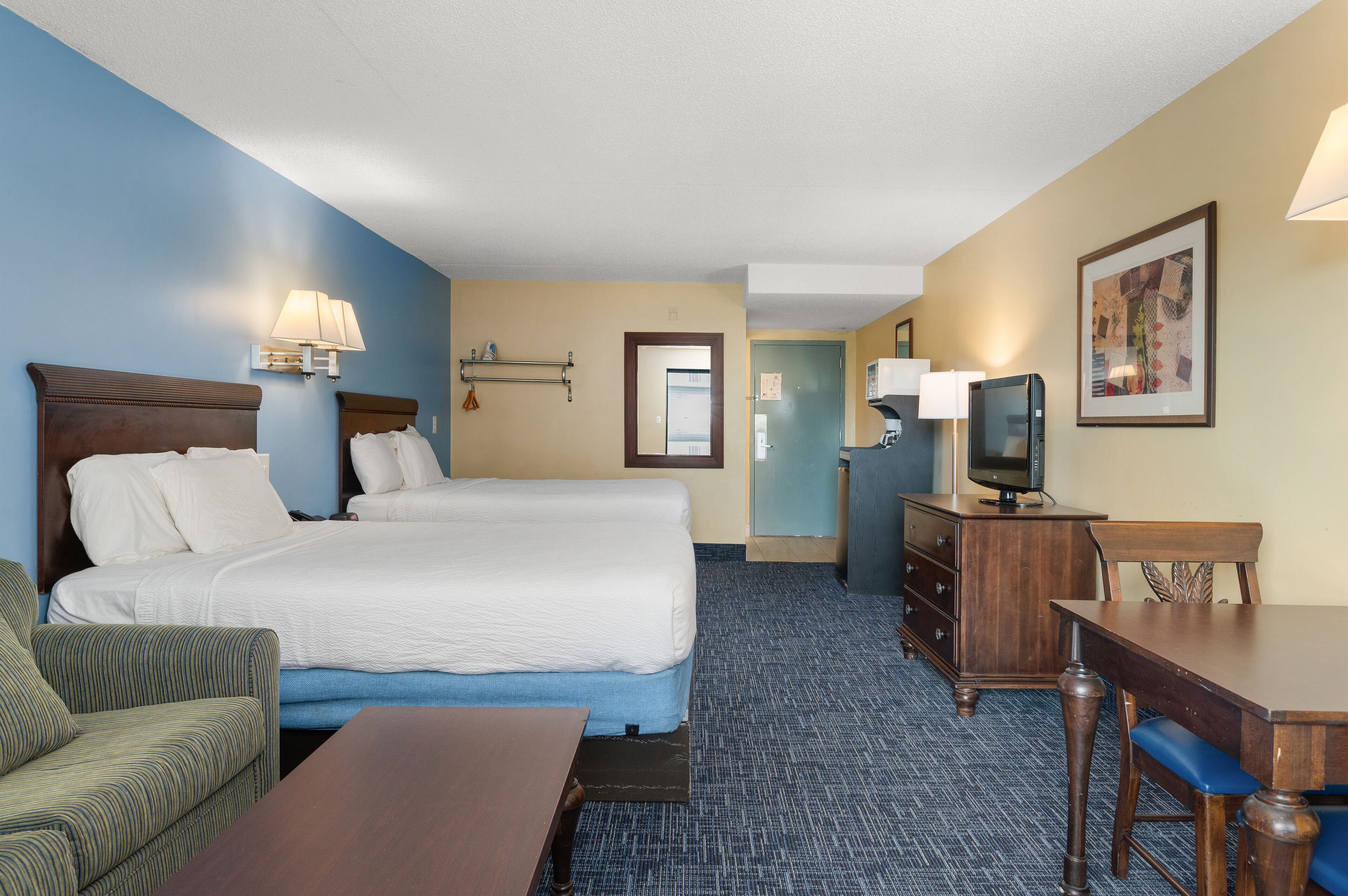 A hotel room with a large bed, a desk, a chair, a television, and a lamp.