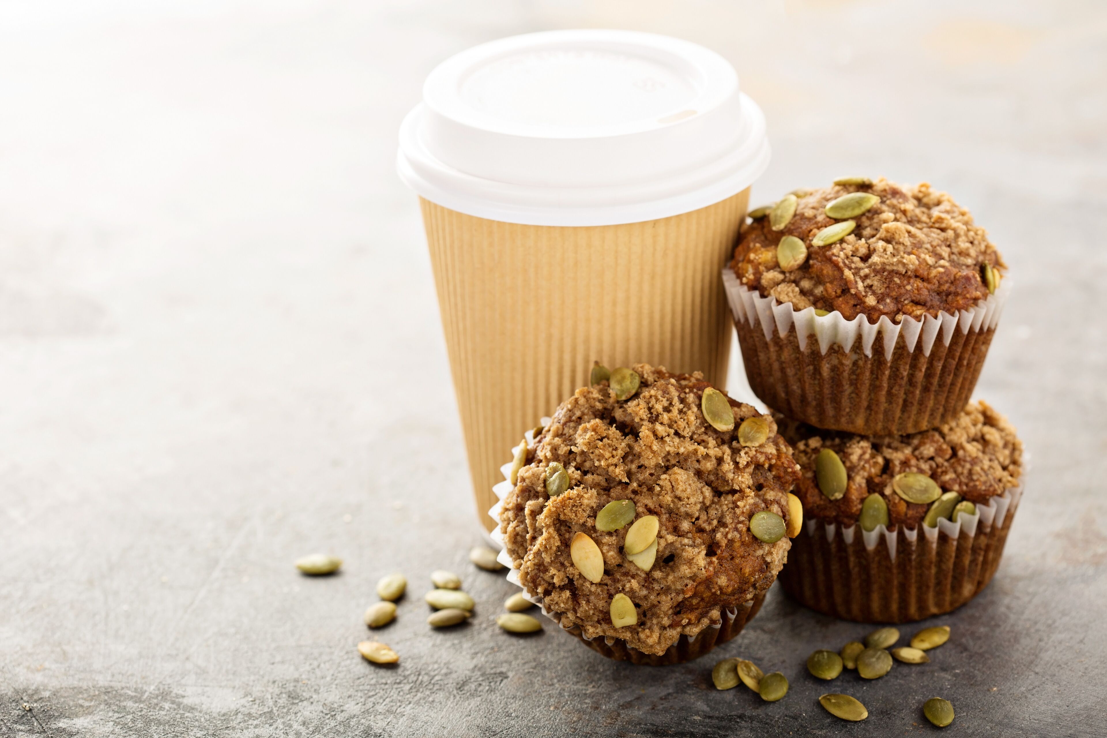 Un montón de muffins con semillas de calabaza y una taza de café con tapa.