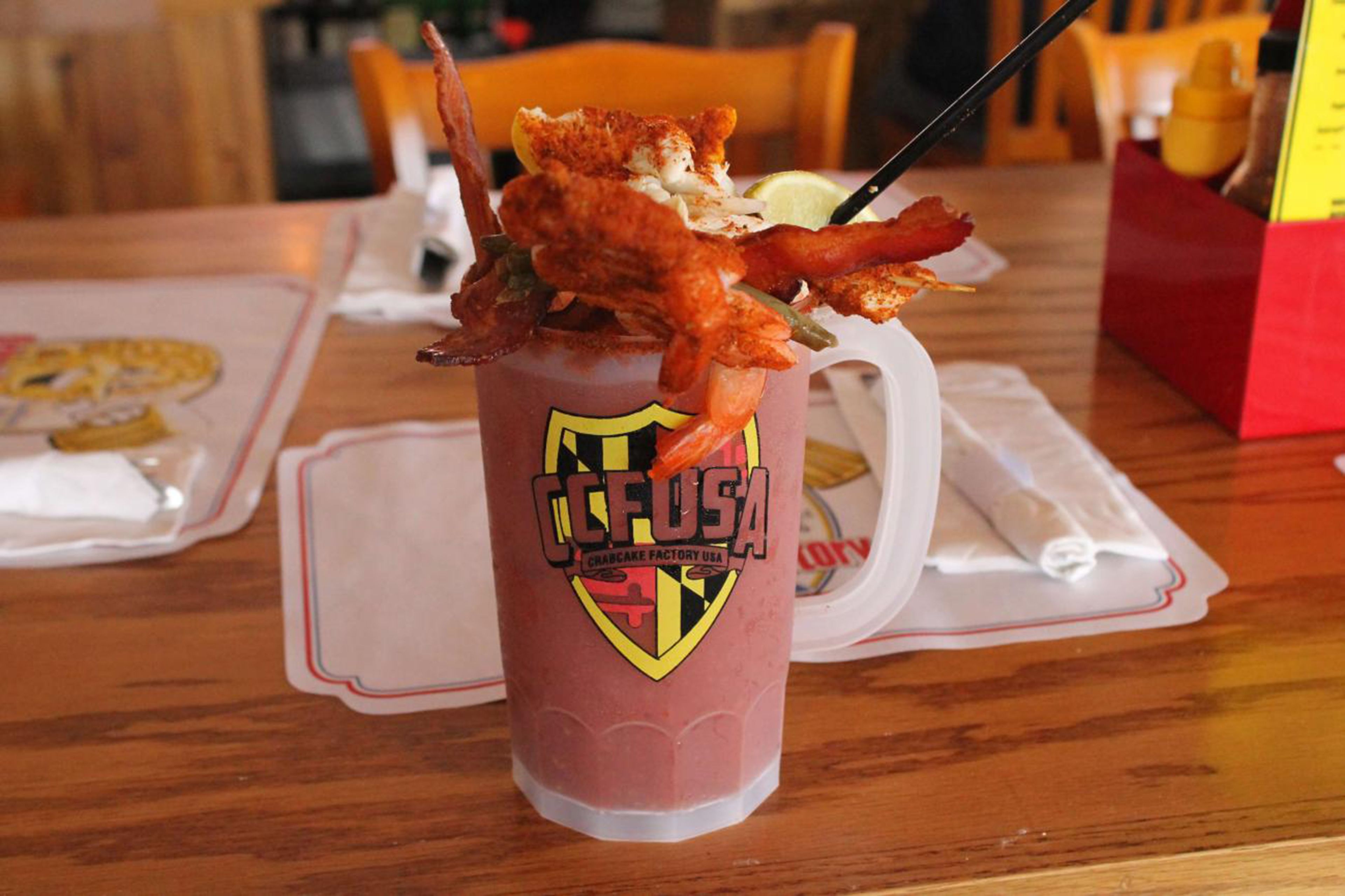 Een drankje met een krab erop, gelabeld 'CCFUSA', op een houten tafel met een witte placemat.