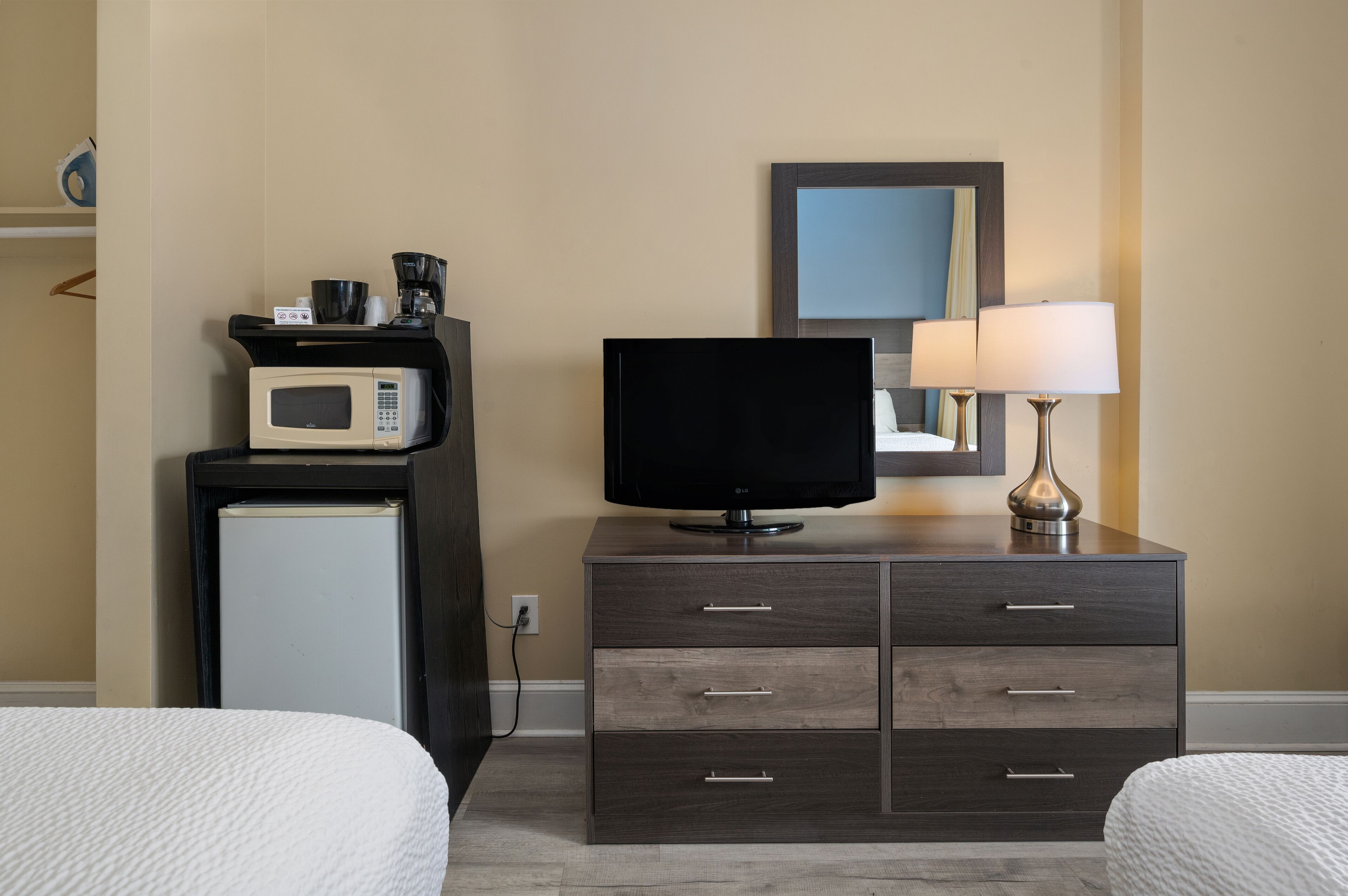 A hotel room with a bed, a TV on a dresser, a microwave, and a lamp.