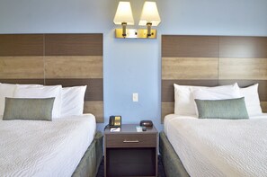 Una habitación de hotel con dos camas, una mesita de noche con lámpara, teléfono y un cajón pequeño.