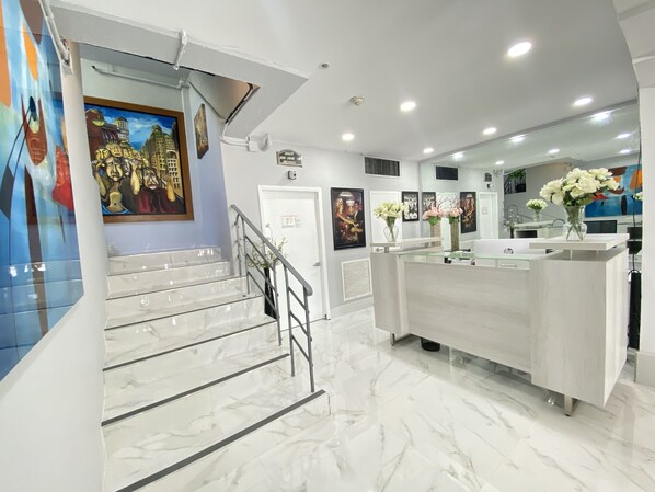A modern hotel lobby with marble floors, a reception desk, and a staircase.