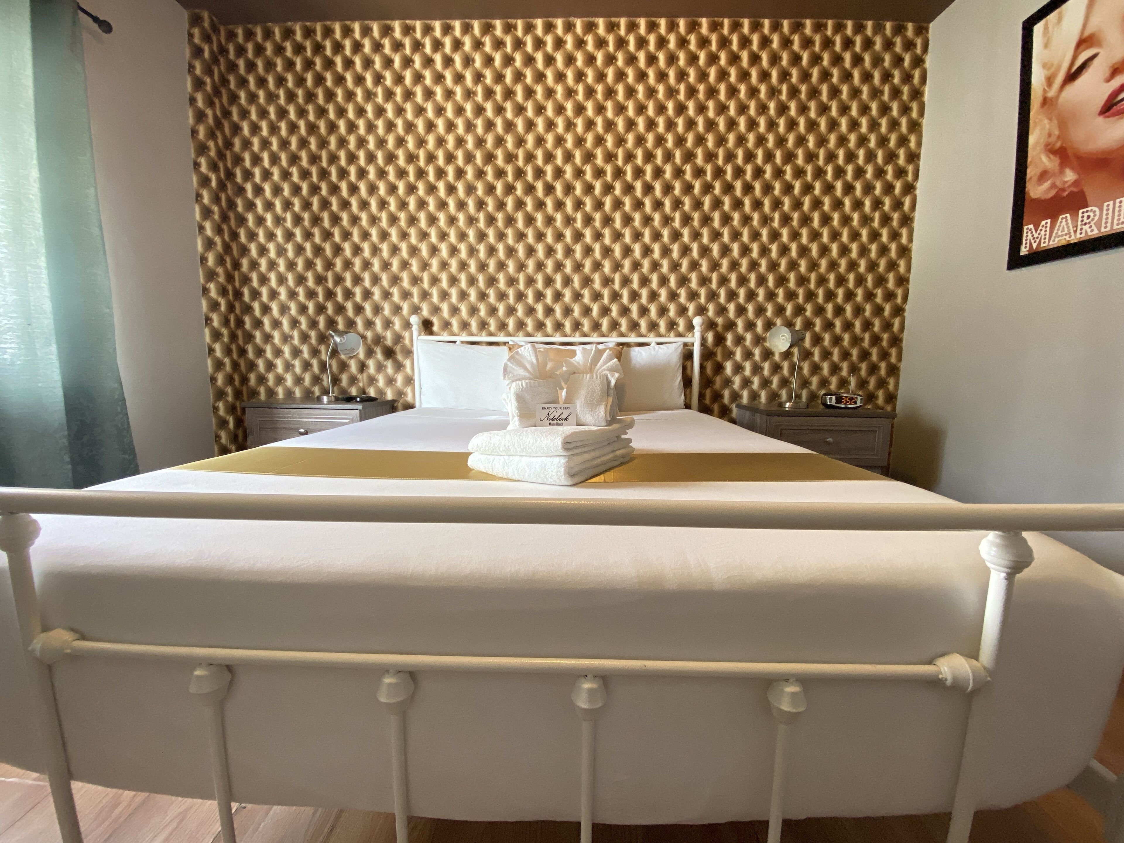 A neatly made bed with a white headboard, a bedside table with a lamp, and a wall with a textured pattern.