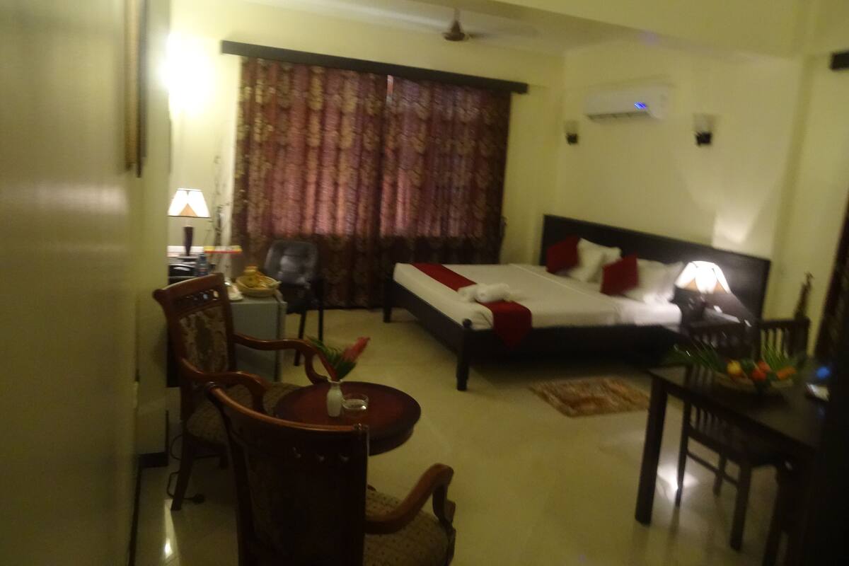 Une chambre d’hôtel avec un lit, un bureau, une chaise, une table et une fenêtre avec des rideaux.