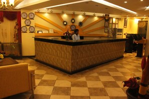 A reception area with a wooden reception desk, multiple clocks, and a check-in counter. - Hotel Sapphire (Dar es Salaam)