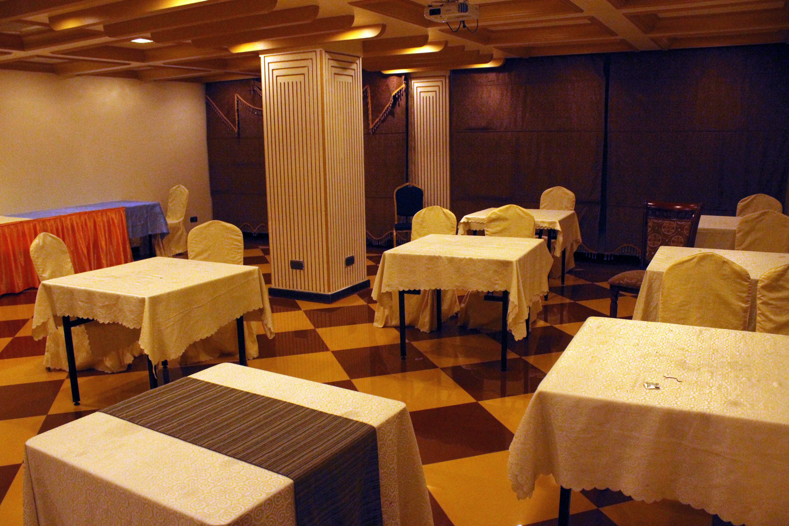 A banquet hall with tables covered in white tablecloths, arranged in rows with chairs.