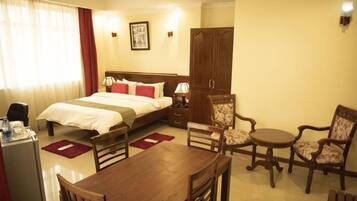 A hotel room with a bed, bedside table, lamp, wardrobe, and a dining area with chairs and a table.