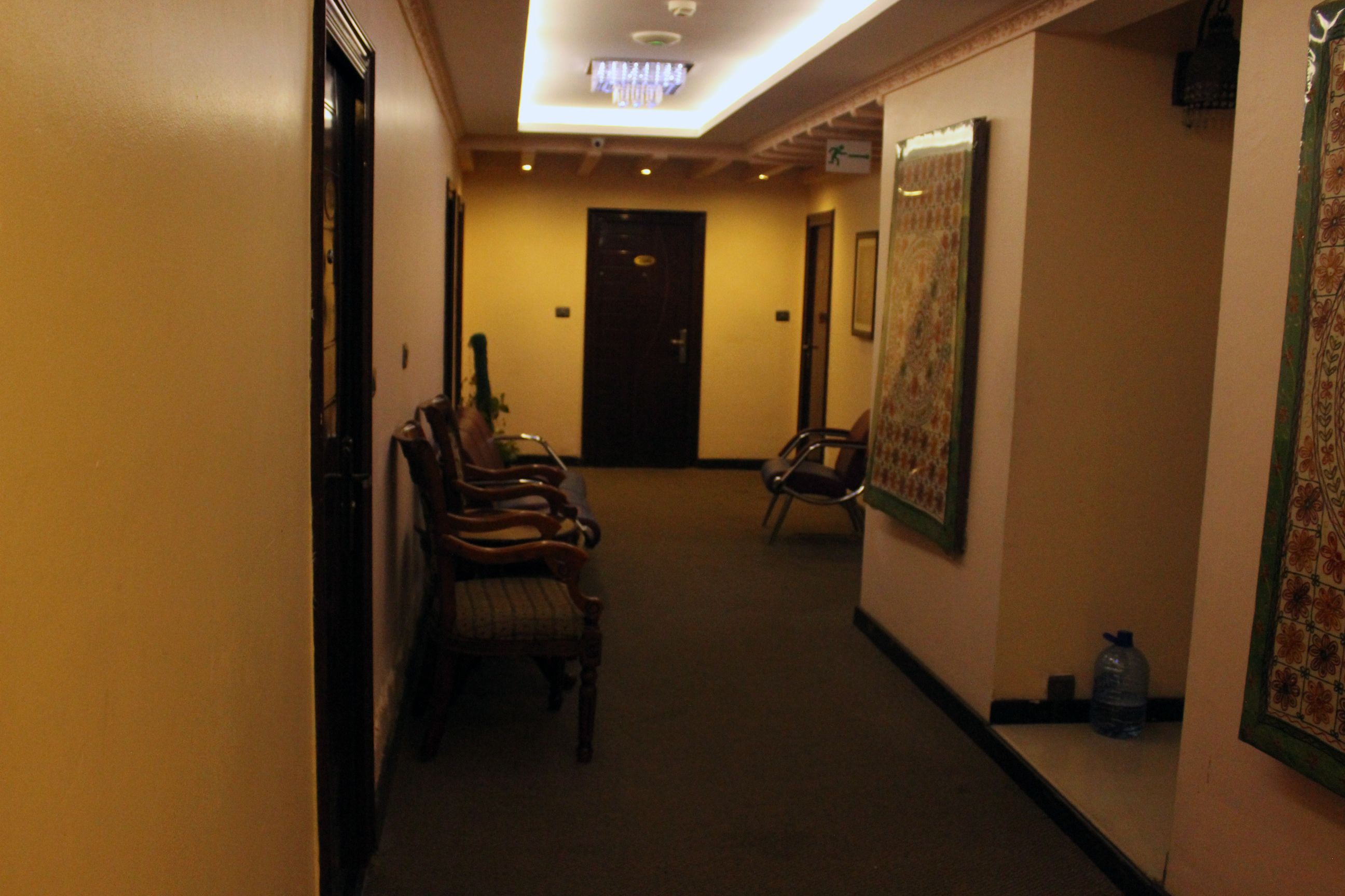 A hallway with wooden chairs, a water dispenser, and a door at the end.