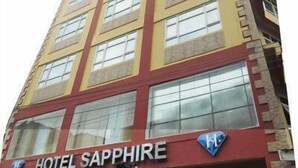Un edificio de hotel alto con varios pisos y ventanas grandes. El nombre del hotel, HOTEL SAPPHIRE, es visible en la fachada.