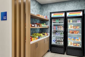 Une boutique aménagée dans une suite d’hôtel, avec des étagères de collations et deux réfrigérateurs pour les boissons.