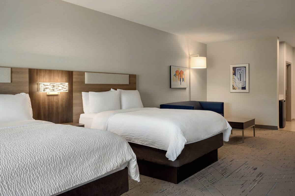 Ein Hotelzimmer mit zwei Betten, einem Holz-Kopfteil, einem kleinen Tisch und Bildern an den Wänden.