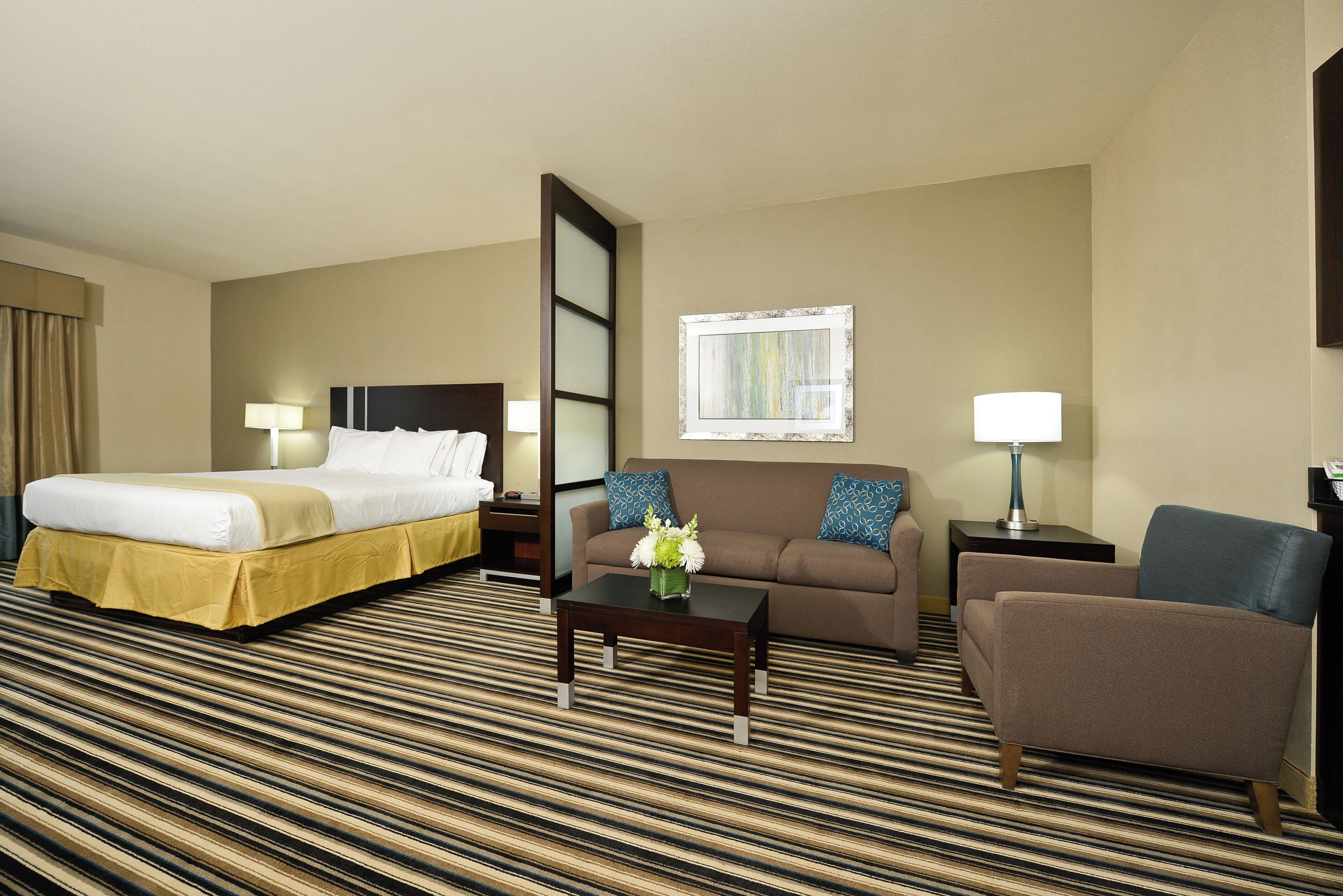 A hotel room with a bed, a sofa, a chair, a coffee table, and a window.