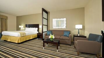 A hotel room with a bed, a sofa, a chair, a coffee table, and a window.