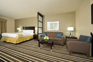 A hotel room with a bed, a sofa, a chair, a coffee table, and a window.