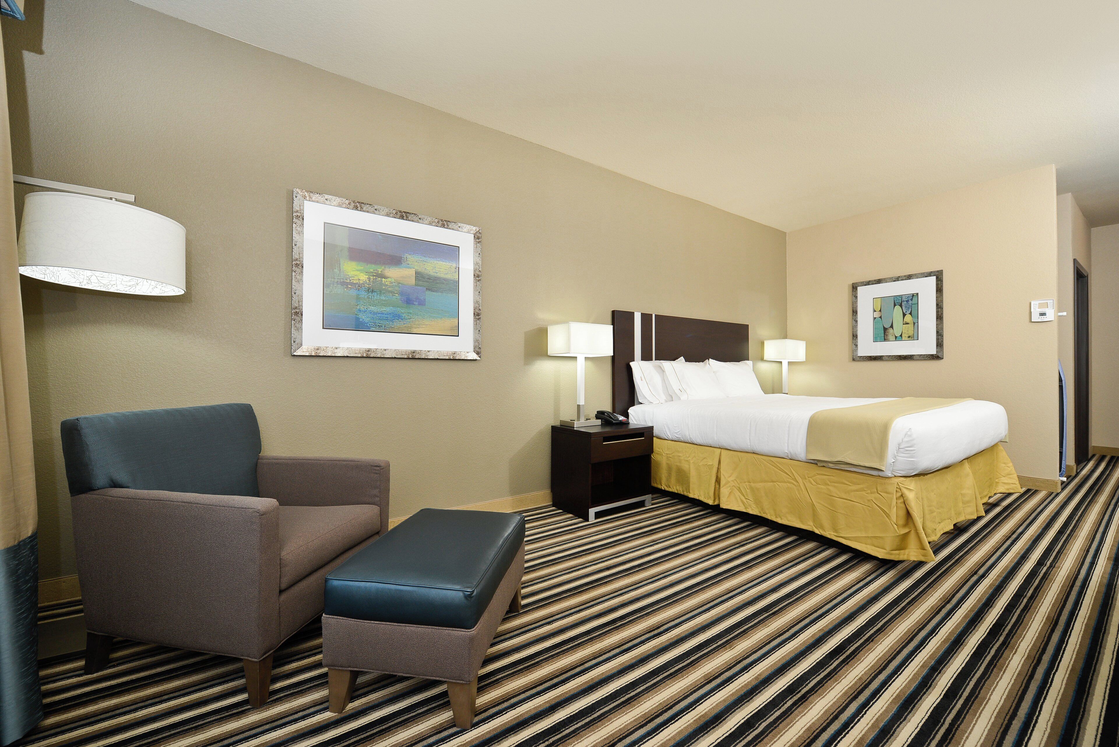 A hotel room with a bed, a chair, a small table, and two wall-mounted lamps.