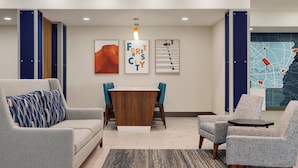 A modern lobby with a gray sofa, a wooden coffee table, and two gray armchairs. There are framed artworks on the wall and a map on the right.