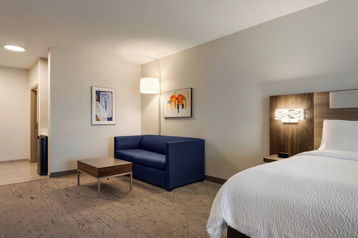 Ein Hotelzimmer mit einem Bett, einem blauen Sofa, einem kleinen Tisch und zwei Wandlampen.