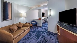 Une chambre d’hôtel avec un canapé marron, un téléviseur à écran plat, un bureau avec une chaise et un sol recouvert de moquette.