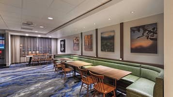 A hotel lobby with a long wooden table, green cushioned seating, and artwork on the walls.