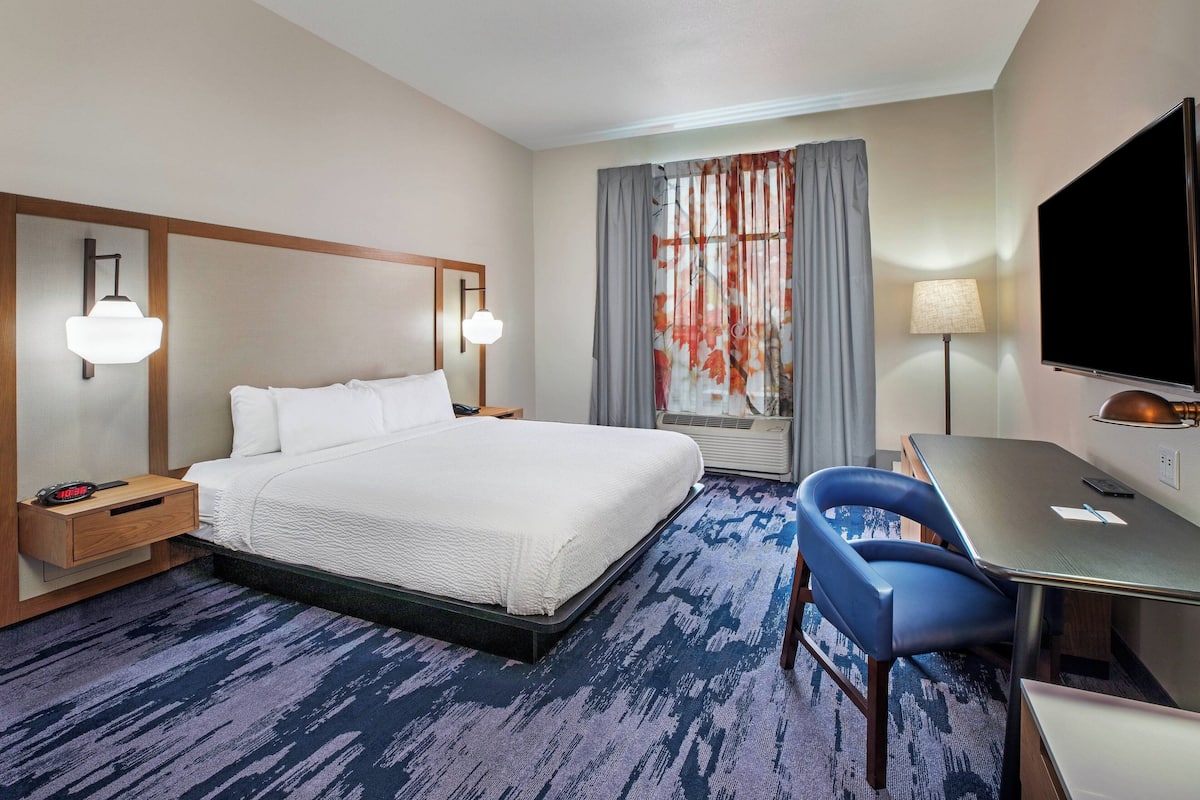 Hotelkamer met een groot bed, een bureau met stoel, een flatscreen-tv, een lamp en een raam met gordijnen.