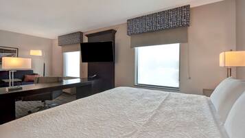 Quarto de hotel com cama grande, escrivaninha, cadeira, televisão na parede e janela com vista.