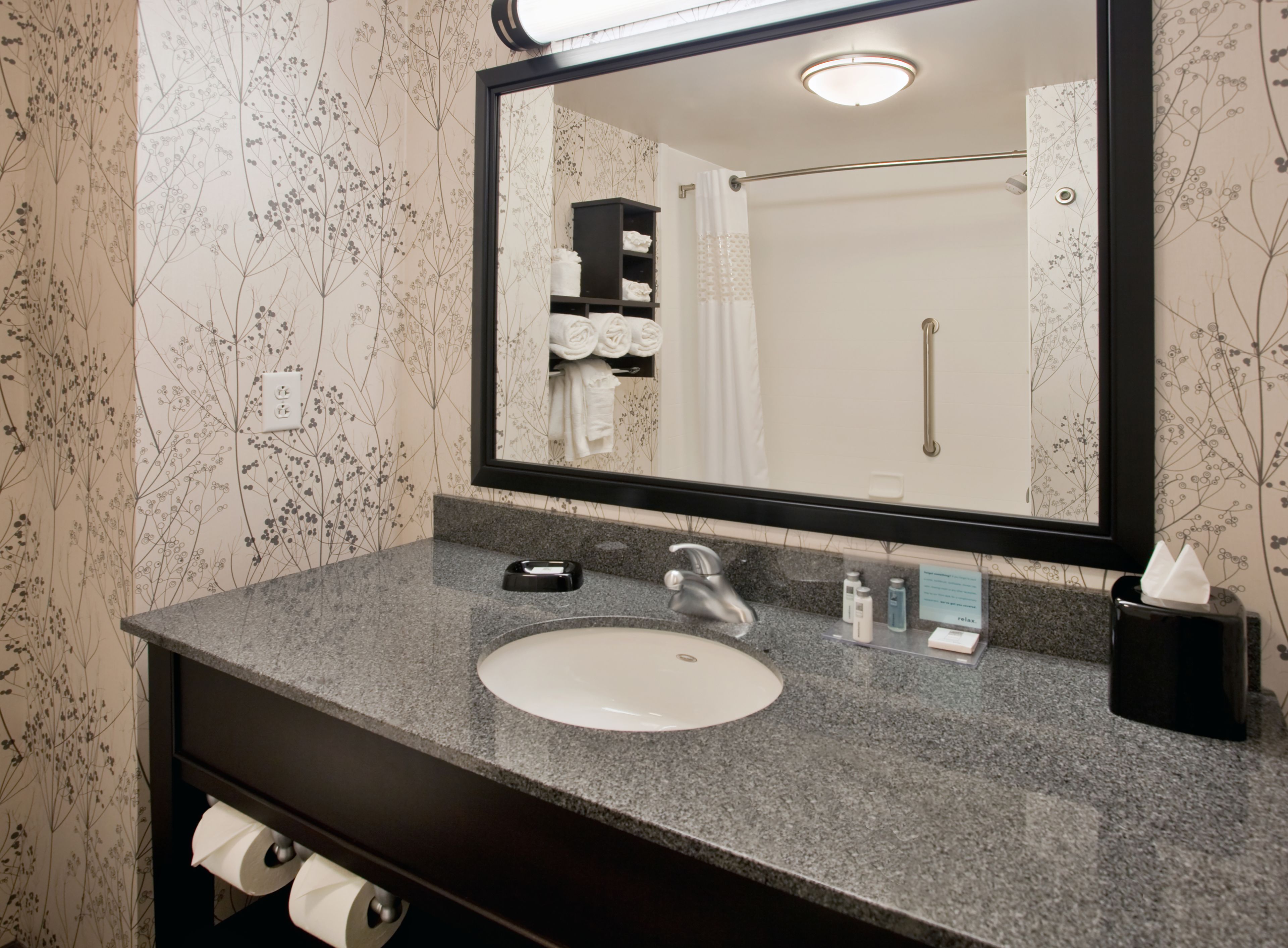 A bathroom with a granite countertop, a white sink, a mirror, and a towel rack with folded towels.