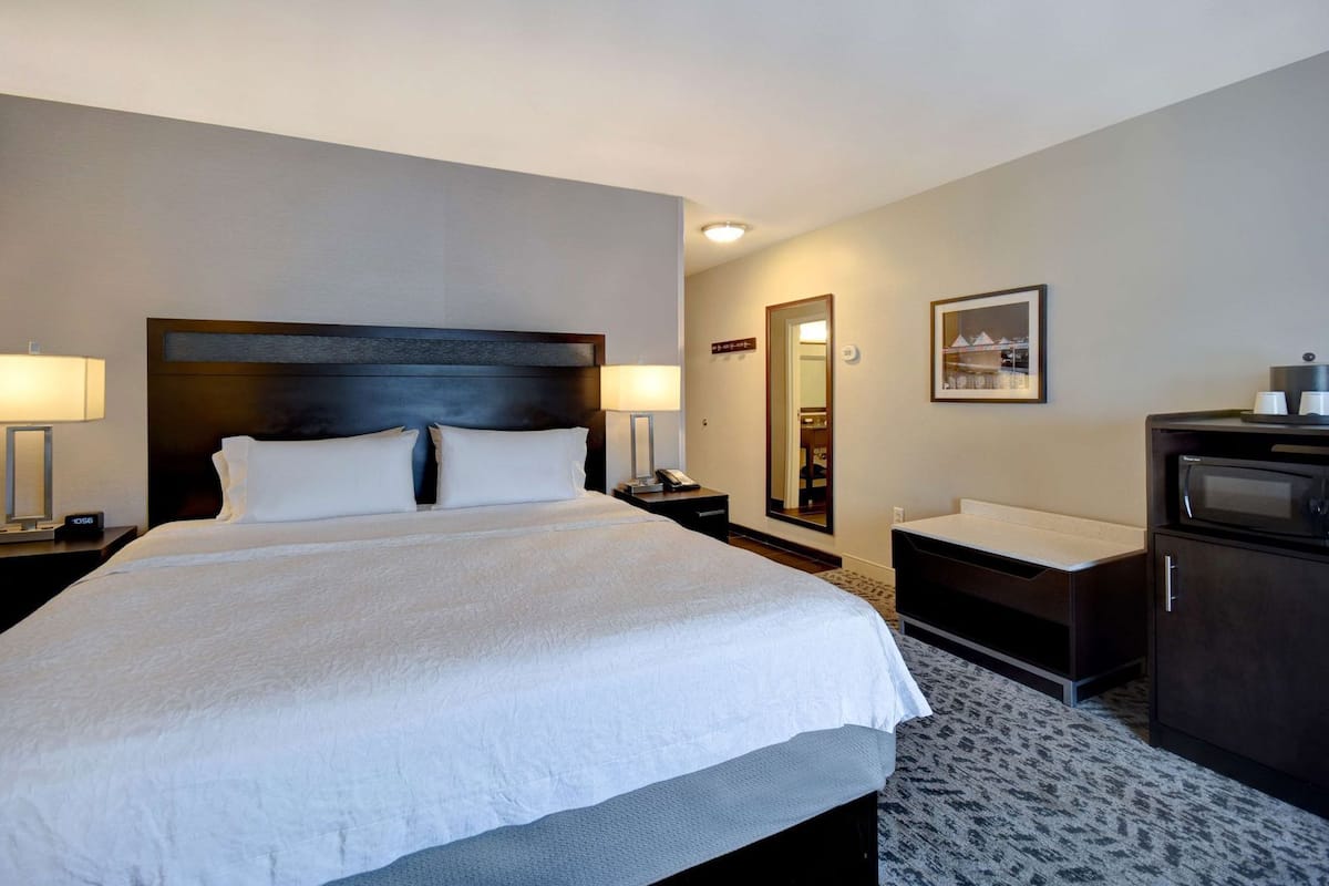 A hotel room with a large bed, bedside tables, a mirror, a dresser, and a microwave.
