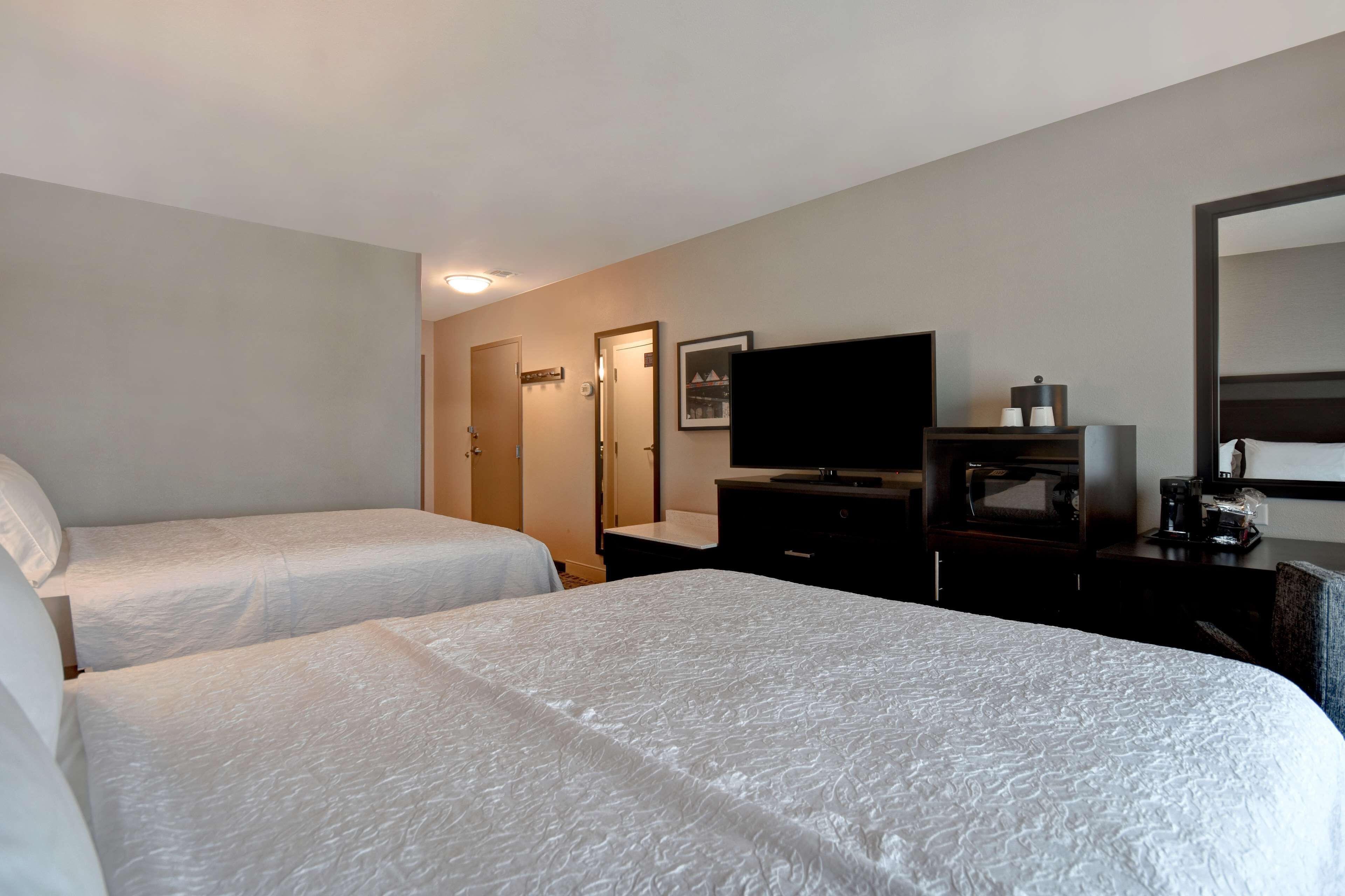 Habitación de hotel con dos camas, televisión, cafetera y espejo.