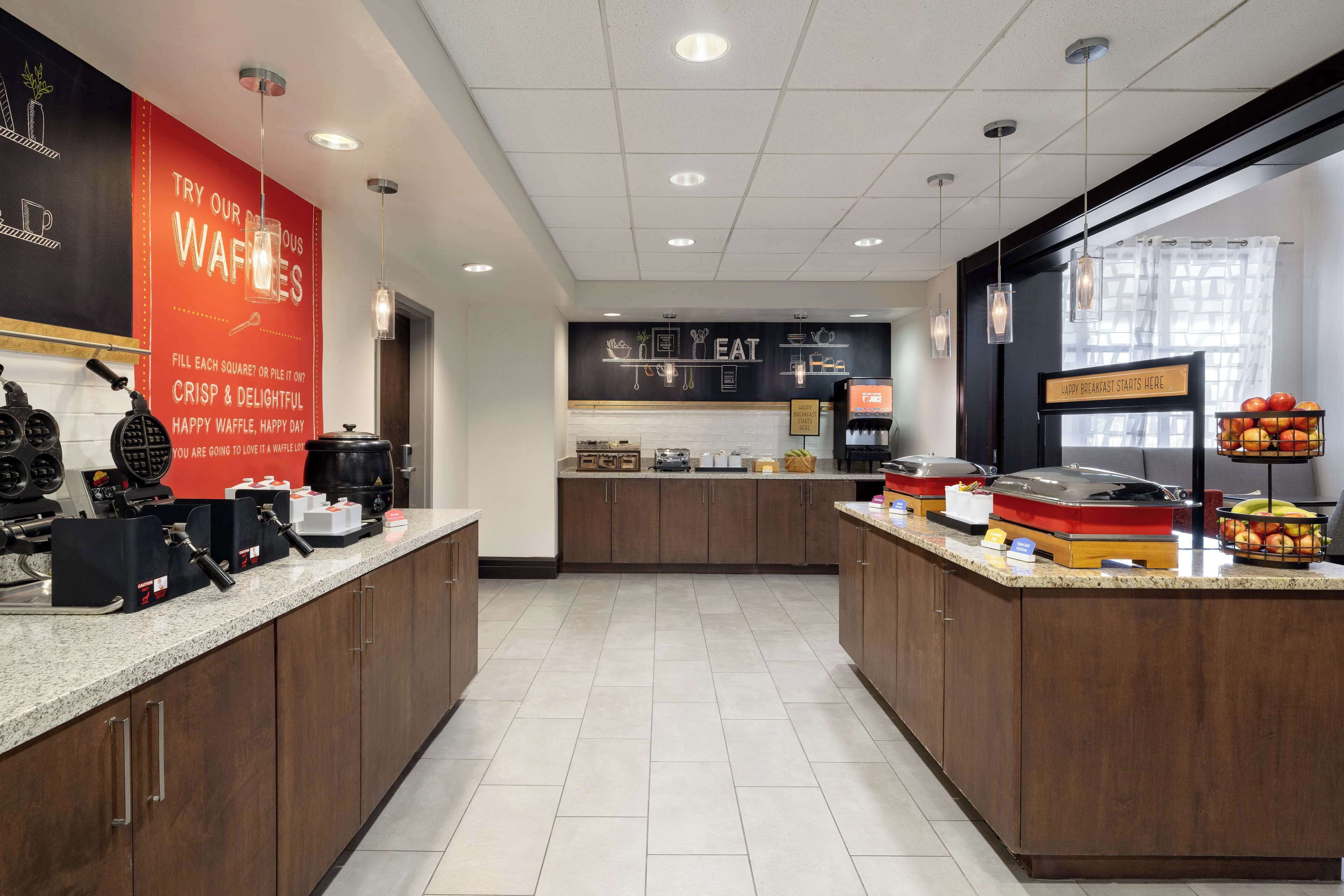 Un espace cuisine moderne équipé de postes pour préparer des gaufres, d’une machine à café et d’un bar pour prendre le petit-déjeuner.