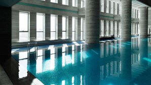 Una amplia piscina interior con agua cristalina y azul, rodeada de ventanas altas y columnas.