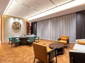A modern hotel room with a round dining table, teal chairs, a sofa, and a large window with curtains. - Pullman Wuxi New Lake (Wuxi)