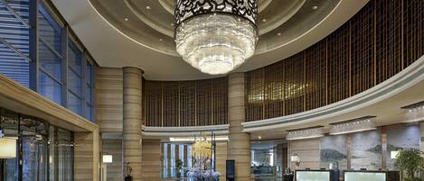 A spacious lobby with a large chandelier, high ceilings, and a central decorative table.