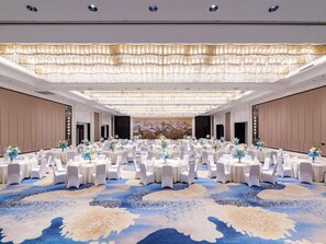 Ein großer Festsaal mit runden Tischen, weißen Stühlen und floralen Tischdekorationen.