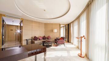 A spacious hotel lobby with a modern design, featuring a large seating area, a reception desk, and a large window with curtains.