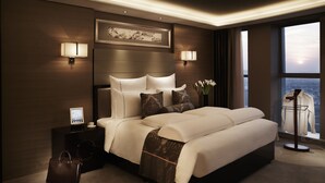 A modern hotel room with a large bed, two bedside tables, a nightstand, a lamp, a vase with flowers, and a view of the city through large windows. - Pullman Wuxi New Lake (Wuxi)