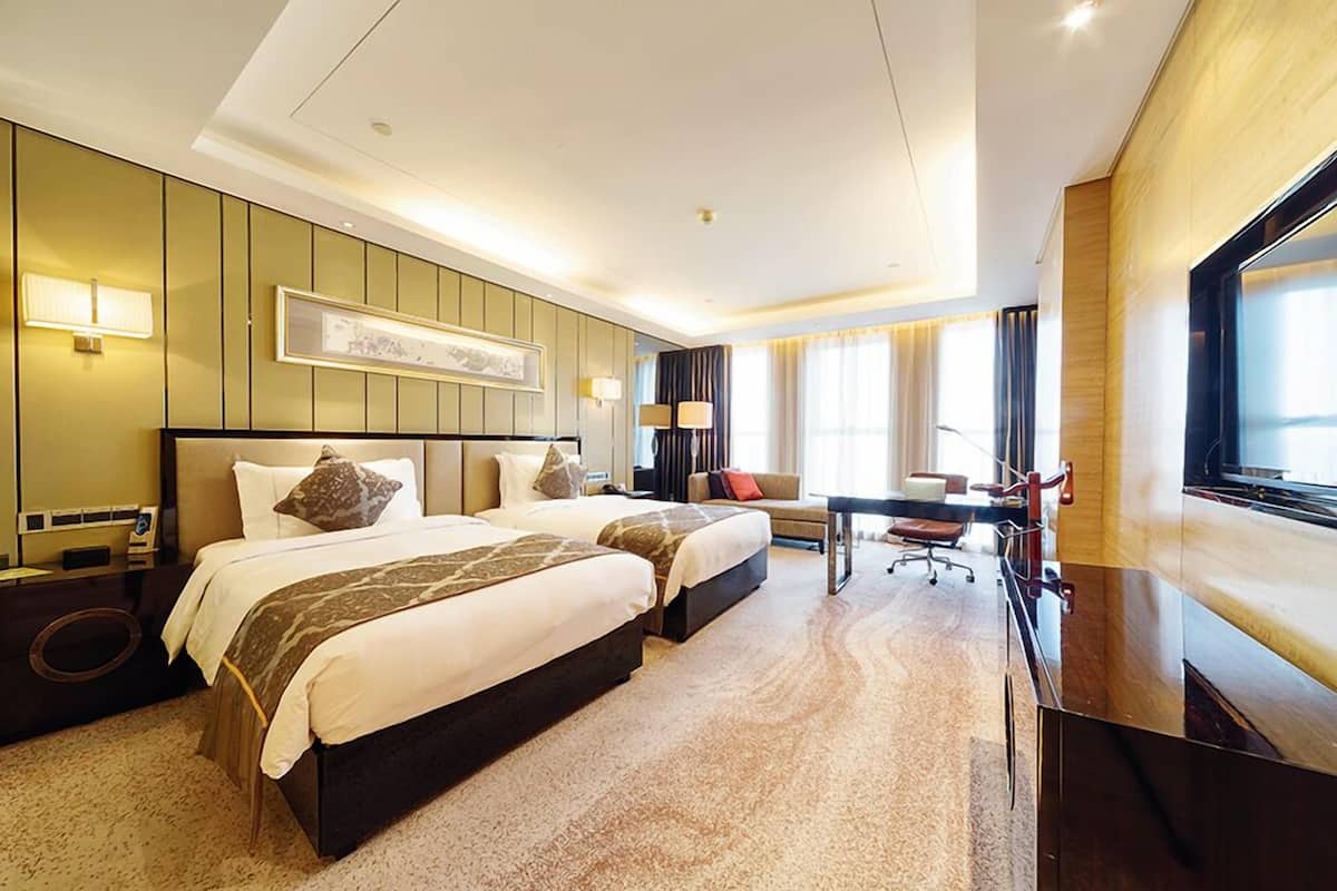 A hotel room with two beds, a desk, and a TV.