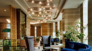 Un vestíbulo amplio con mobiliario moderno, una planta grande y una lámpara decorativa en el techo.