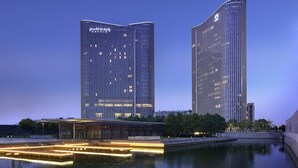 Dos edificios altos con ventanas iluminadas, una fuente en primer plano y un edificio moderno con zona cubierta.