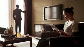 A living room with a sofa, a coffee table with a tray of items, a television, and a person standing by a window. - Pullman Wuxi New Lake (Wuxi)
