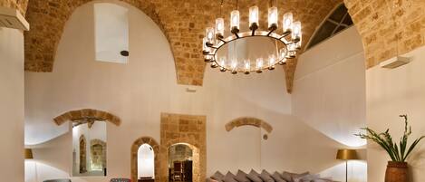 A spacious lobby with a high arched stone ceiling, a central chandelier, and a modern seating area with sofas and chairs.