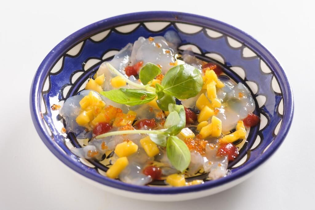 A bowl of food with mango chunks and basil leaves.