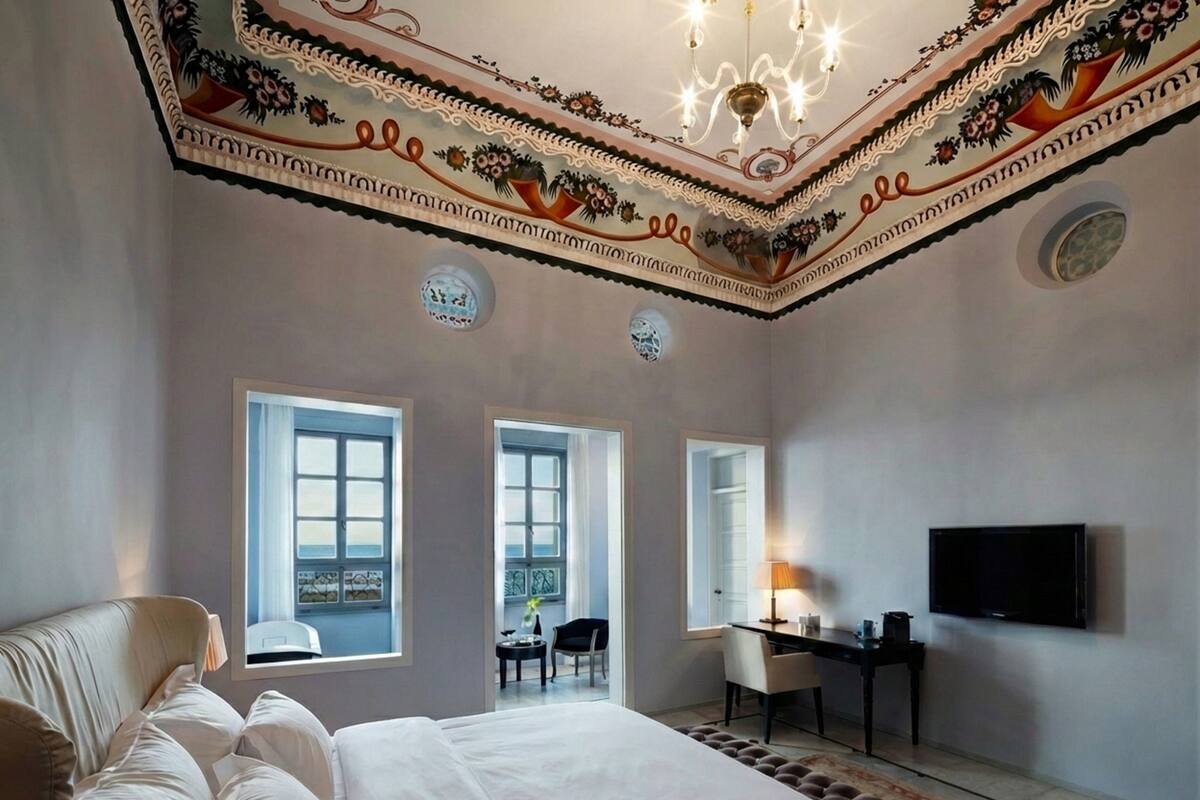 A hotel room with a large bed, a desk, a chair, a TV, and a balcony with a view.